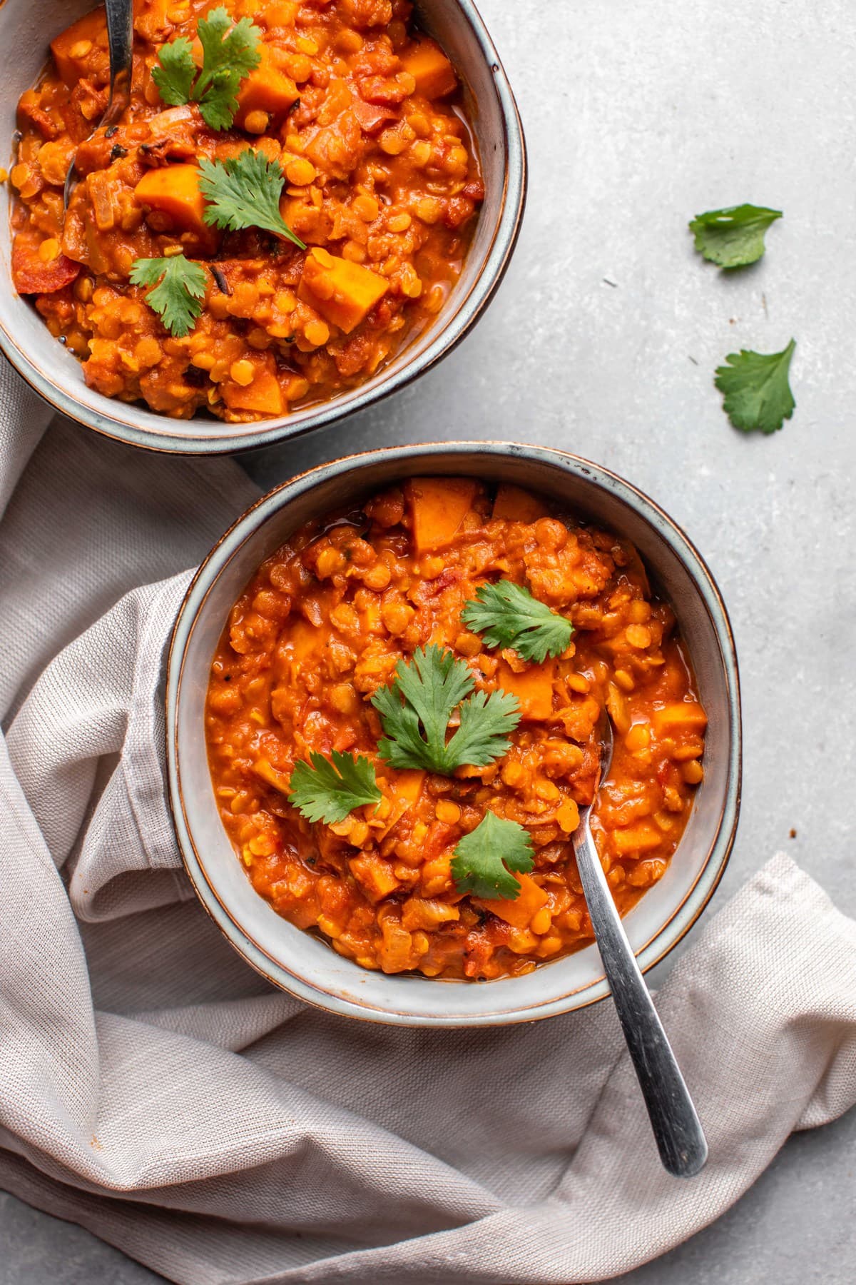 two bowls of sweet potato stew topped with cilantro on grey background