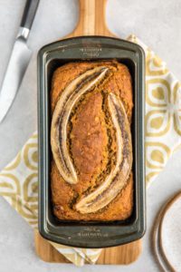 loaf of baked banana bread in baking tin on white stone background