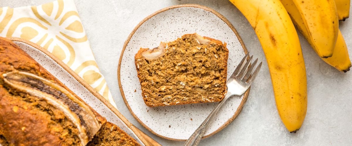 slice of vegan banana bread on white speckled plate on light gray background