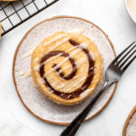 Stack of cinnamon roll pancakes on small white plate on marble background