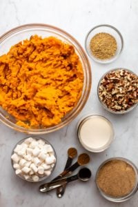 ingredients for sweet potato casserole in small glass bowls on marble background