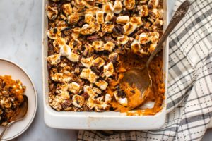 sweet potato cassrole in white casserole dish with marshmallows pecans and serving spoon