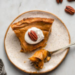 slice of pecan and pumpkin custard pie on white speckled plate with bite taken out of it on marble backgrond
