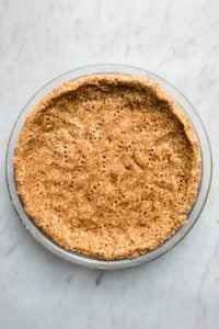 pecan and date crust in glass pie tin on marble background