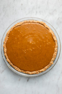pumpkin filling added to glass pie pan before baking on marble background