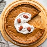 pumpkin and pecan custard pie with coconut whip and pecans in glass pie tin on marble background