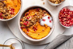 sweet potato breakfast bowl topped with granola, coconut yogurt, and pomegranate seeds