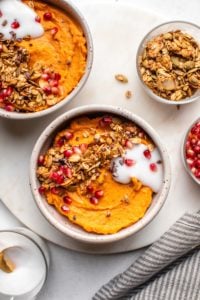 two sweet potato breakfast bowls topped with coconut yogurt, pomegranate seeds, and granola