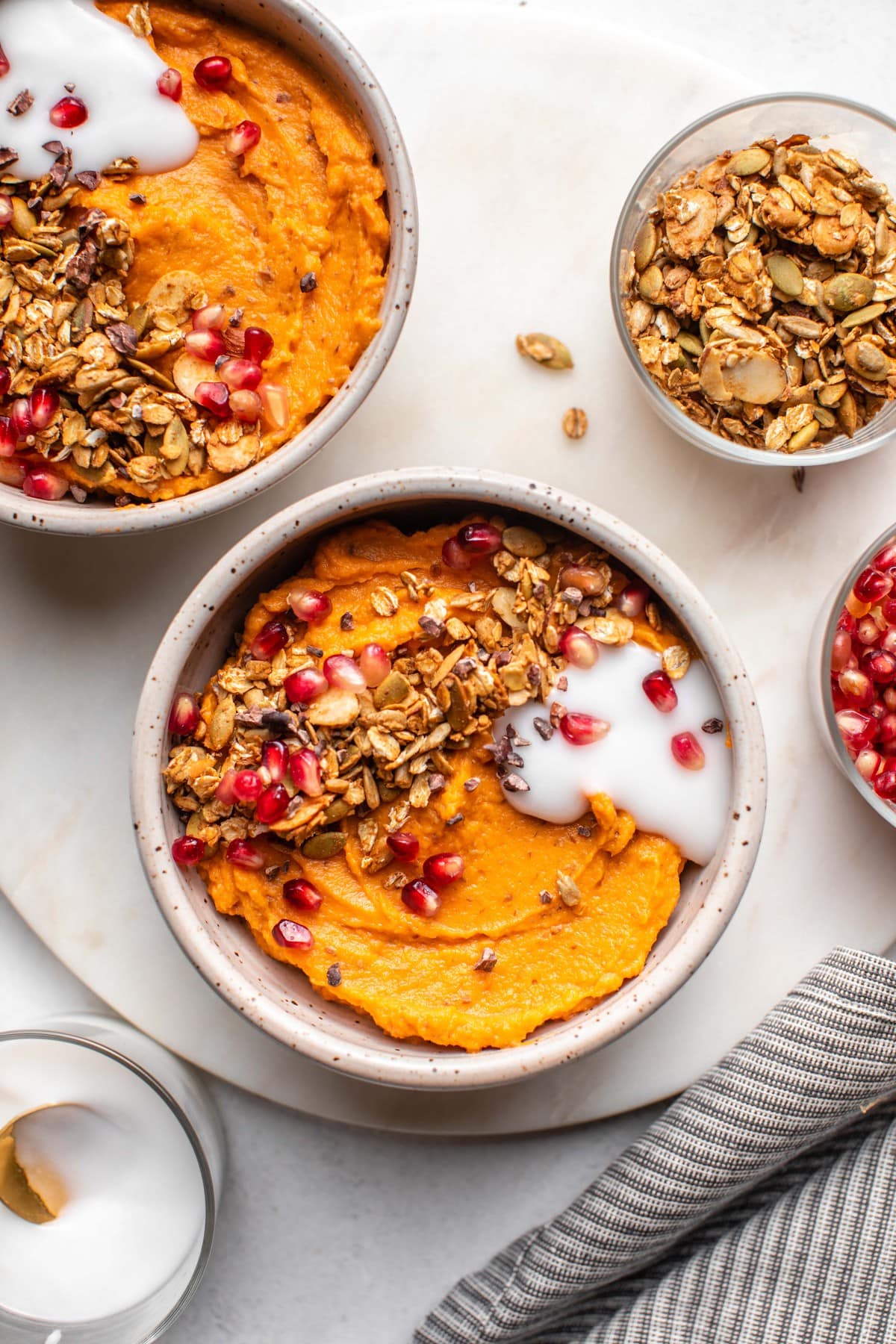 two sweet potato breakfast bowls topped with coconut yogurt, pomegranate seeds, and granola