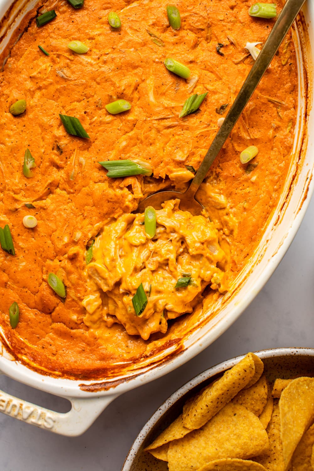 a spoon scooping up a serving of vegan buffalo chicken dip from a white baking dish