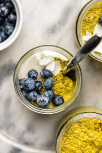 glass jar of golden milk chia seed pudding with silver spoon on marble background