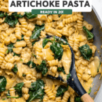Cooked spinach artichoke pasta in large pan with spoon scooping pasta out