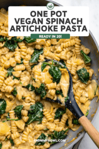 Cooked spinach artichoke pasta in large pan with spoon scooping pasta out