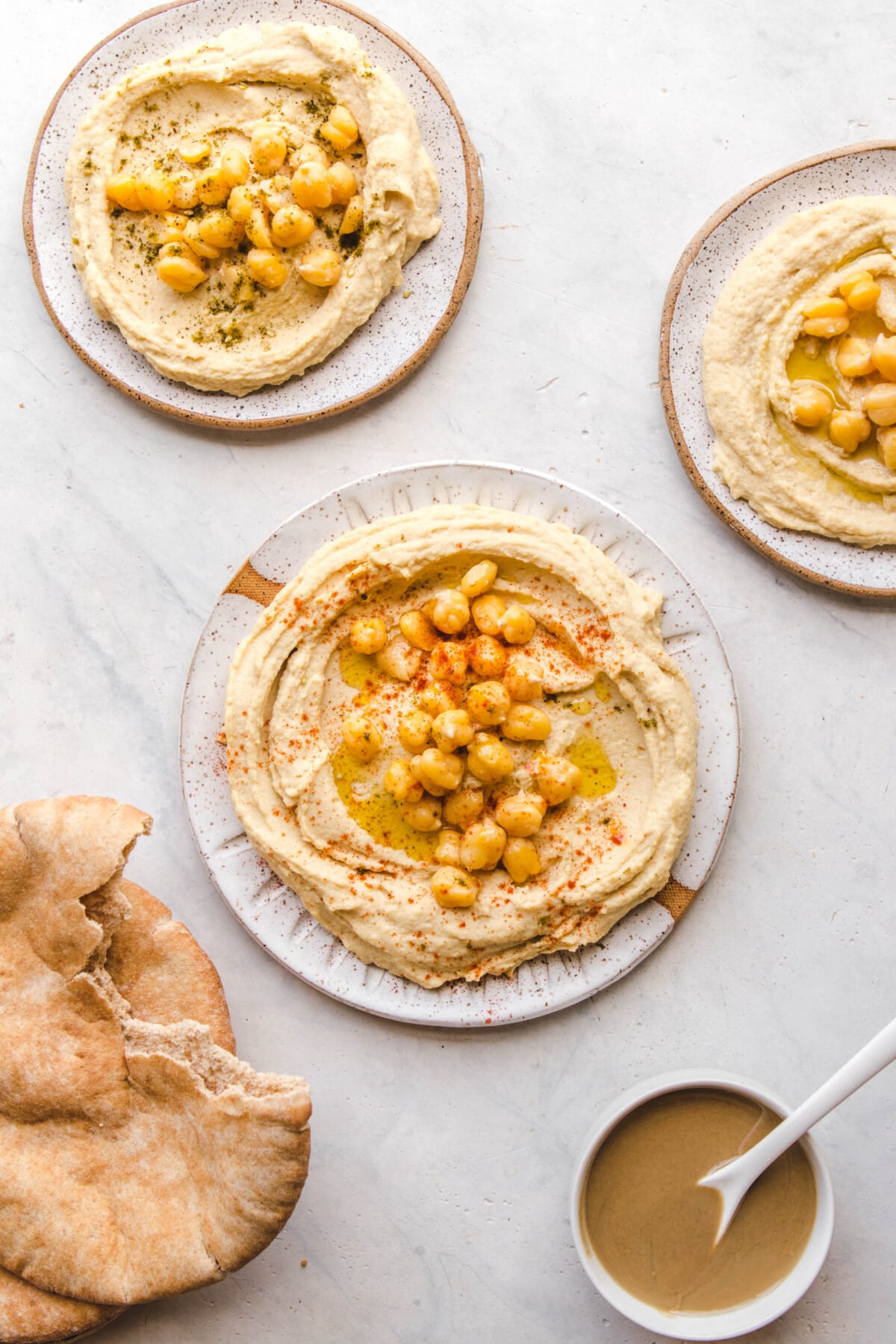3 plates of hummus with pita bread and tahini on the side