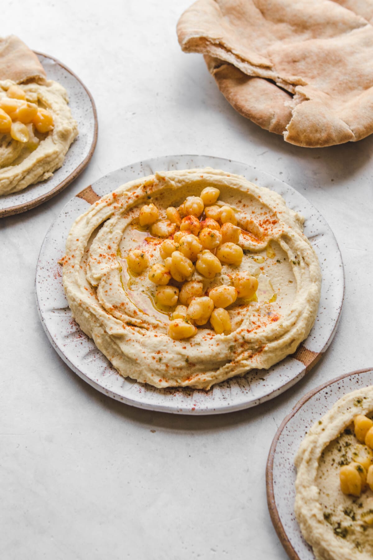 3 plates of hummus topped with olive oil and chickpeas with pita bread off to the side