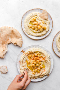 hand dipping into plate of hummus with pita bread