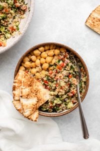 Bowl of quinoa tabbouleh with chickpeas and sliced pita bread