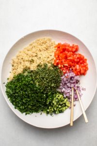Ingredients for quinoa tabbouleh arranged in large white bowl, separated before mixing