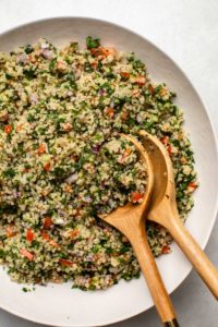Mixed quinoa tabbouleh in large white bowl with two wooden serving spoons