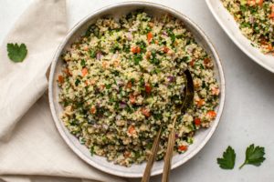 Quinoa tabbouleh in white bowl with spoon on marble background