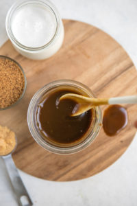 spoon mixing salted caramel sauce in glass jar on wood cutting board
