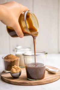 pour shot of salted caramel sauce into glass jar on wood cutting board
