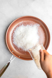 coconut shreds being poured into nonstick pan