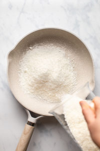pouring untoasted coconut into nonstick pan