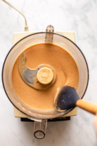 spatula stirring smooth coconut butter in food processor on marble background