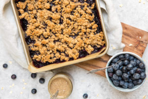 blueberry crumble bars in pan with fresh blueberries and almond butter