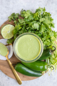 overhead shot of creamy cilantro dressing in glass jar with ingredients on wood cutting board