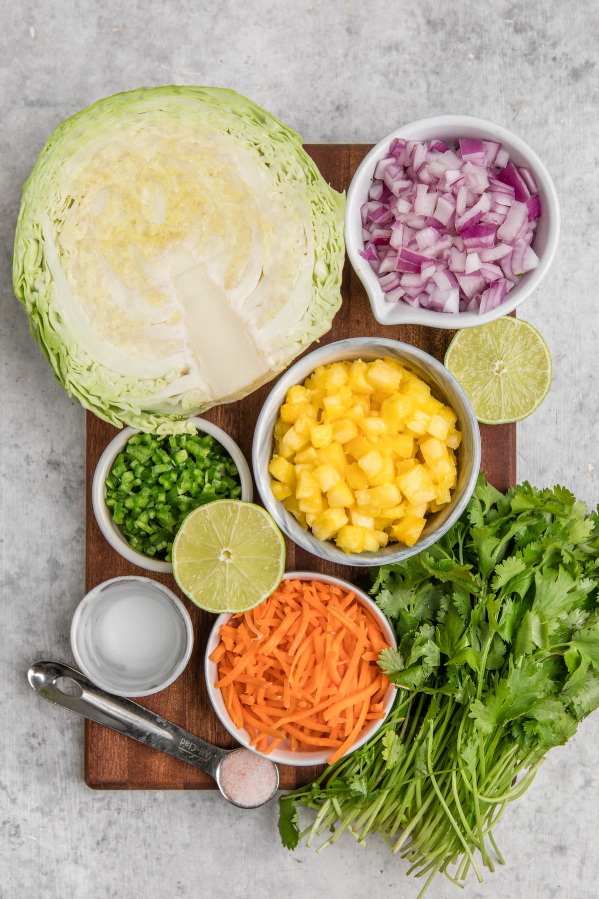 wood cutting board holding all of the pineapple coleslaw ingredients