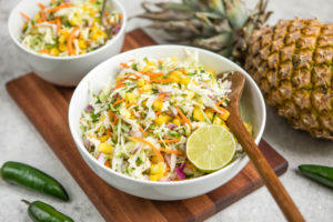 white bowl of pineapple coleslaw with wood spoon