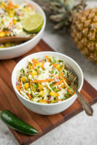 small bowl of pineapple coleslaw on wood cutting board