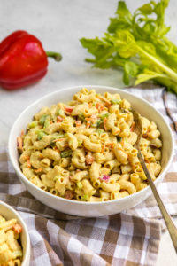 large white bowl of macaroni salad with veggies in the background