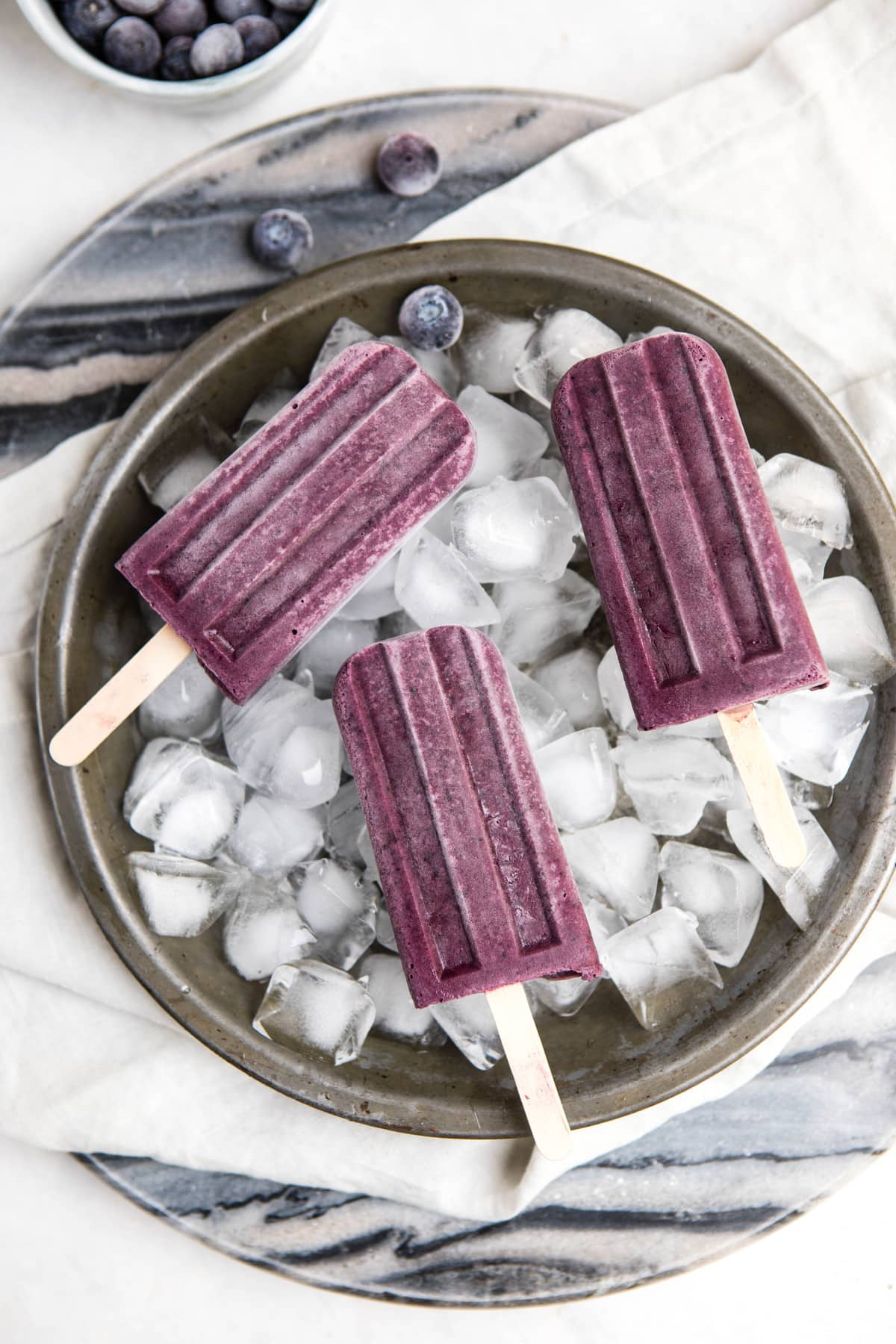 3 blueberry maqui popsicles on round tray of ice