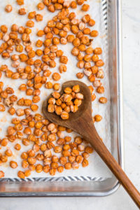 baking sheet covered in crispy buffalo chickpeas and wooden spoon