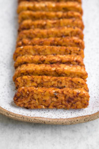 close up shot of cooked smoky tempeh on white serving platter