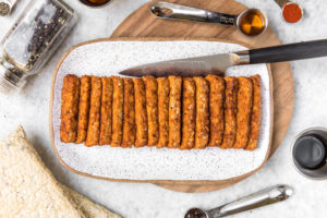 smoky tempeh on white serving platter surrounded by ingredients to prepare tempeh