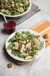 quinoa and arugula salad on white plate with walnuts