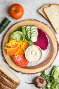 spread of rainbow vegetables, hummus, and bread on white backdrop