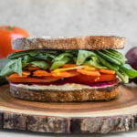 rainbow veggie sandwich on round wood cutting board