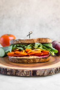 rainbow veggie hummus sandwich on round wood cutting board