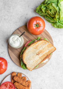 overhead photo of vegan blt on wood cutting board with tomatoes and lettuce on the side