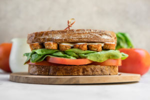 vegan blt sandwich on round wood cutting board
