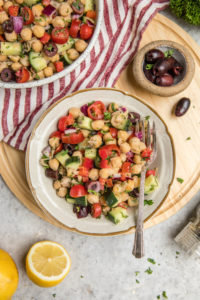 white bowl of chickpea salad with red and white striped napkin and grey background