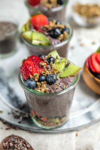 glass jar of acai chia pudding topped with granola, strawberries, kiwi, and blueberries