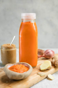 Bottle of carrot ginger dressing surrounded by ingredients on wood cutting baord