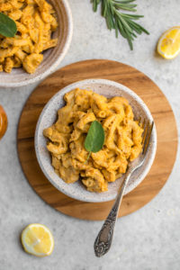 white bowl of pumpkin pasta on wood cutting board with lemon wedge