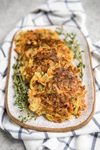 crispy root vegetable pancakes lined on white serving tray with fresh thyme